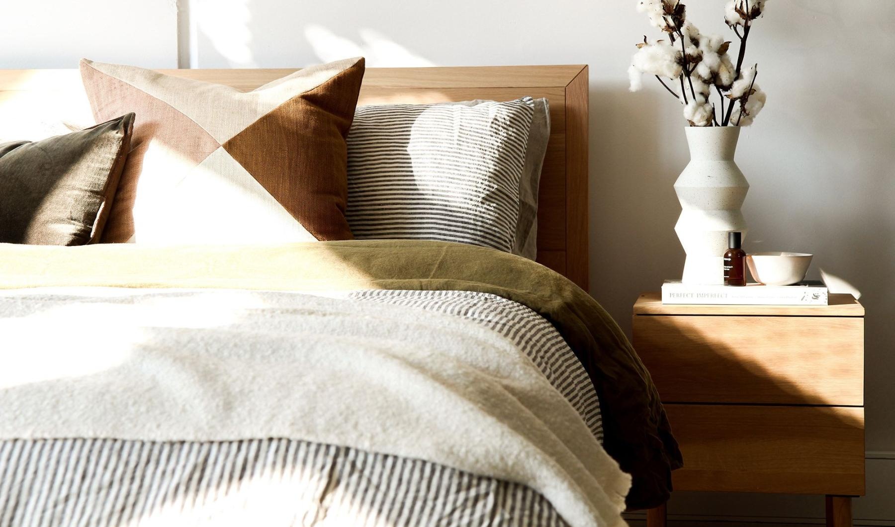 swath of sunlight shines across a well made bed and bedside table with a vase of cotton plants
